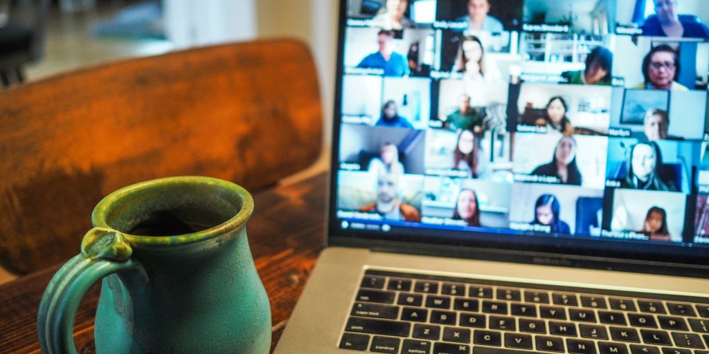 Laptop displaying a virtual meeting with multiple participants, featuring a coffee mug in the foreground, illustrating remote collaboration and communication strategies.