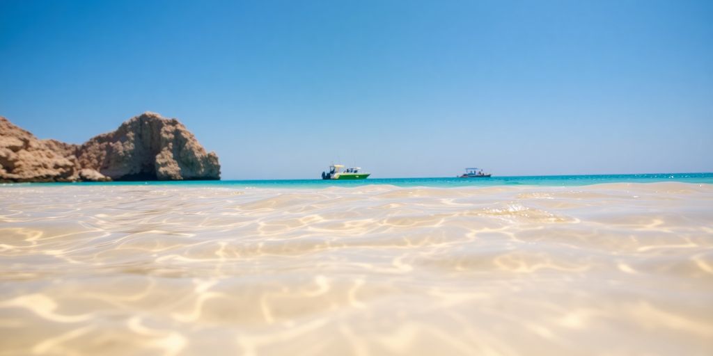 Sun-drenched beach with clear water, distant boats.