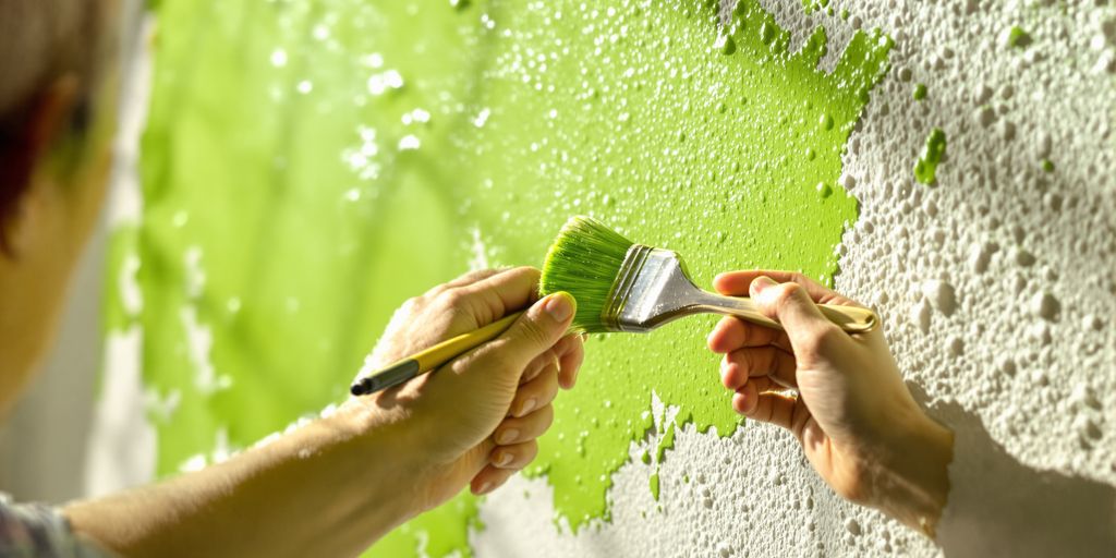 Hands painting a wall with green paint.