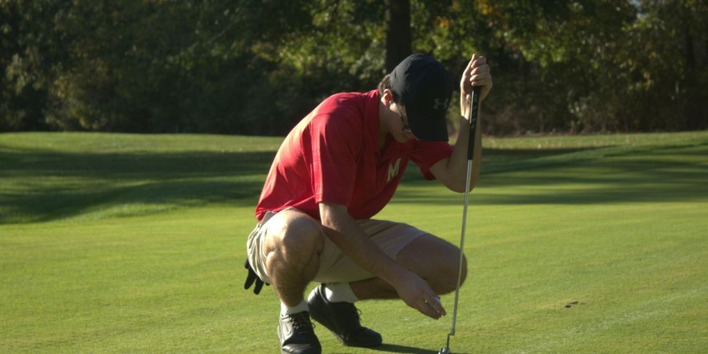 A man kneeling down to put a golf ball in the hole