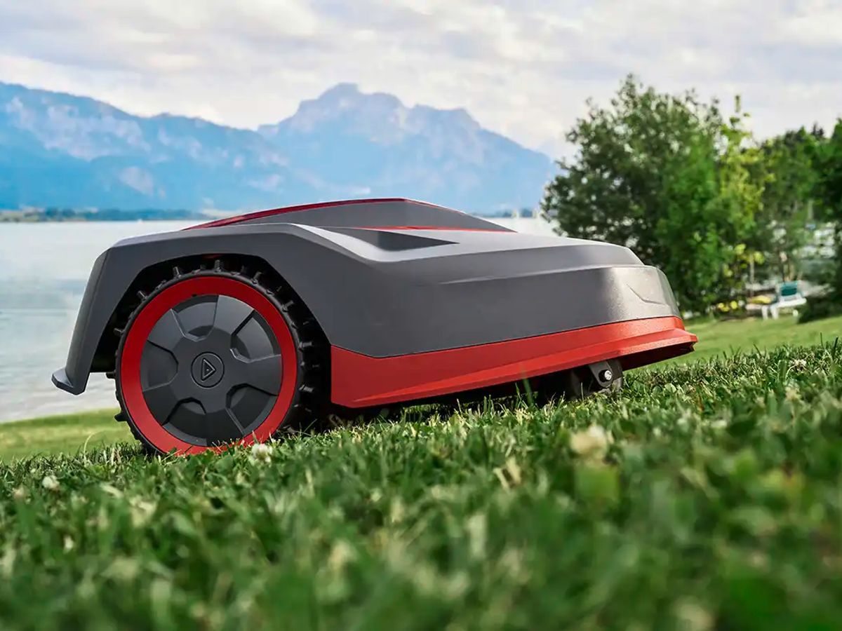 A robotic mower on grassy terrain near a lake.
