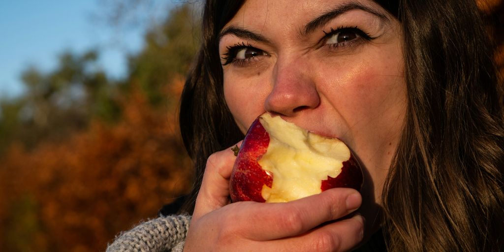 woman in gray sweater holding sliced of apple