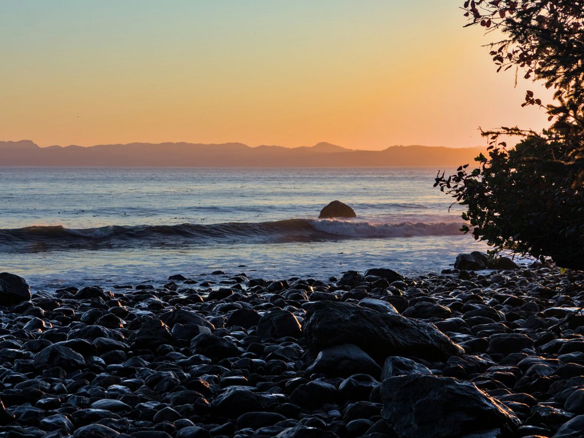 the sun is setting over the ocean with rocks on the shore