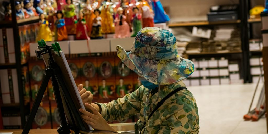 a woman in a hat is painting on a easel