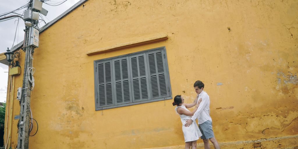a man and a woman kissing in front of a yellow building