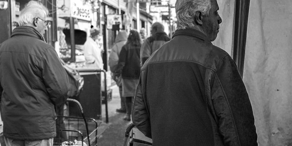man in black jacket standing near people walking on street in grayscale photography