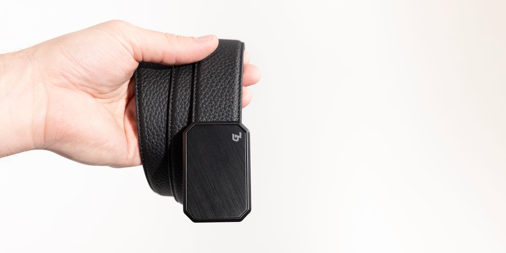 A hand holding a stylish black belt with a sleek buckle.