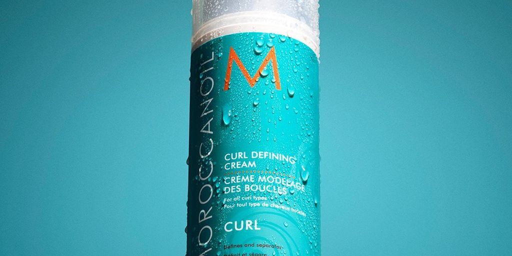 Bottle of curl-defining cream with water droplets on surface.