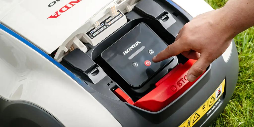 A hand pressing the start button on a Honda mower.