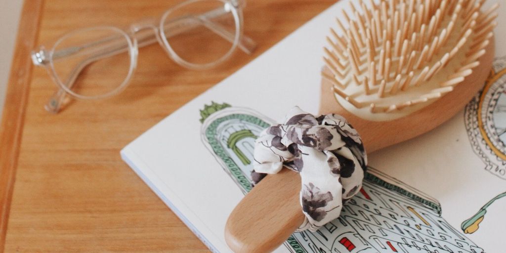 Wooden hairbrush, eyeglasses, and a patterned scrunchie on a book.