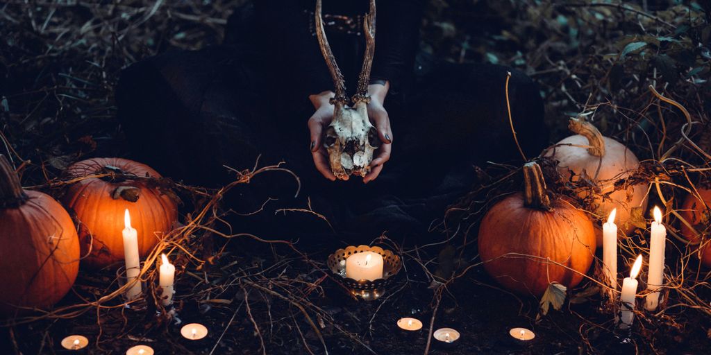 person holding cattle skull surrounded by squash and candles