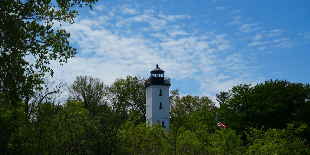 A white light house sitting on top of a hill
