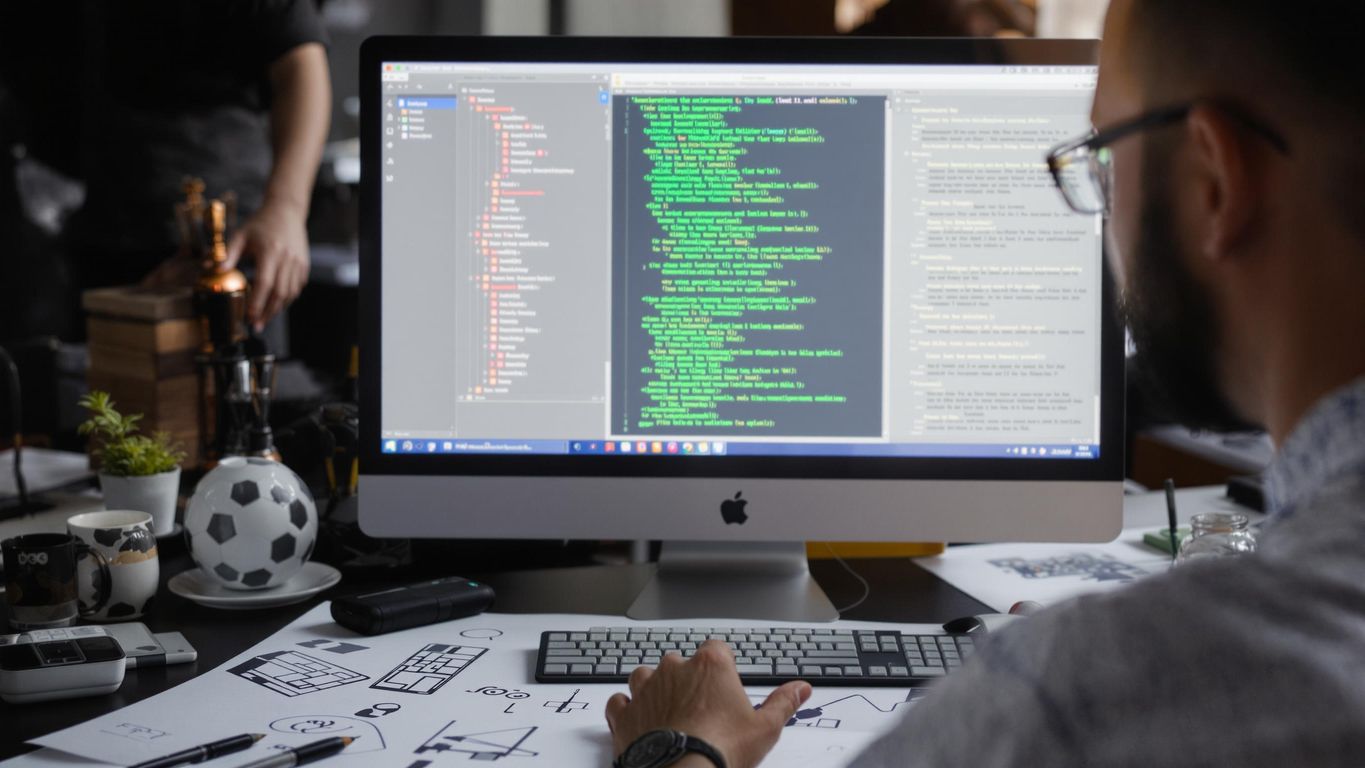 Webutvikler som jobber med datamaskin og designskisser.