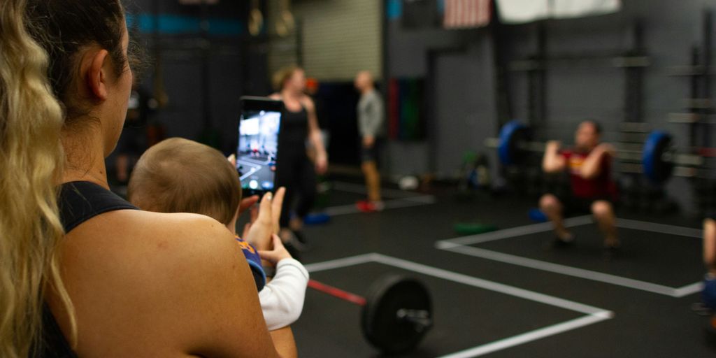 woman carrying baby while using smartphone inside gym