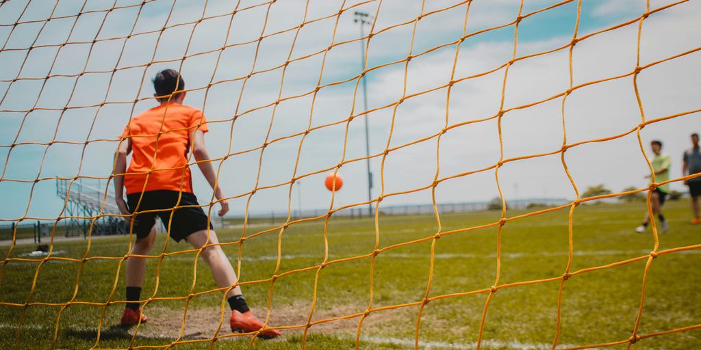 boy in orange shirt and black shorts playing soccer during daytime