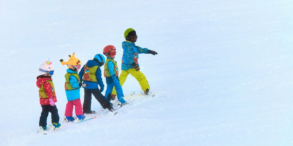 a group of young children riding skis down a snow covered slope