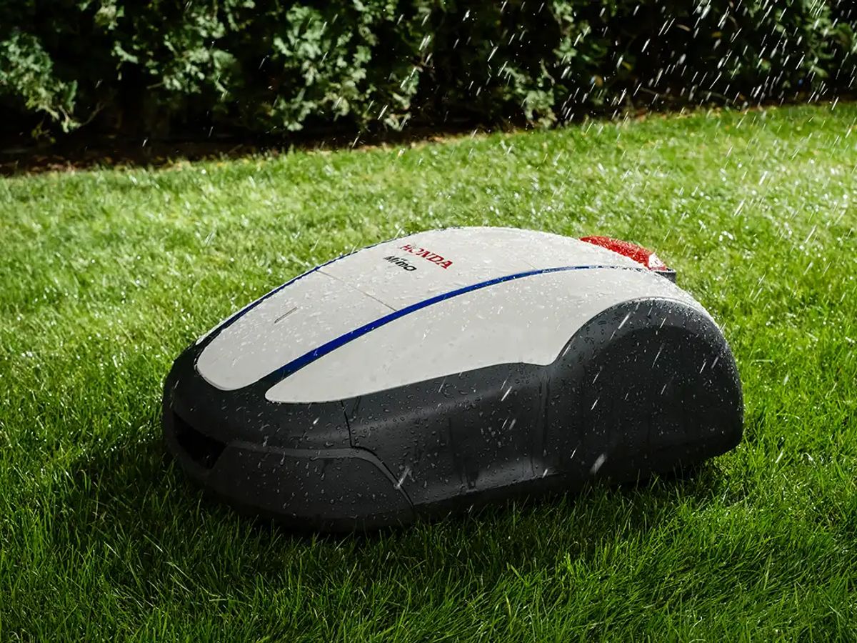 Robotic lawn mower cutting grass in light rain.
