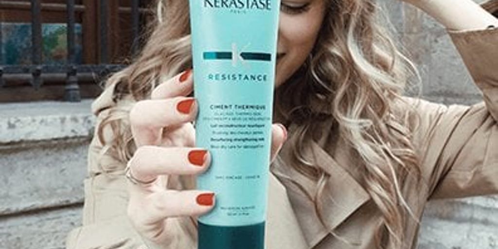 Person holding a Kerastase hair product with a subtle smile.