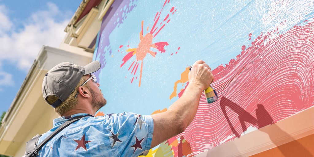 Painter applying colorful paint on a house exterior on a sunny day.
