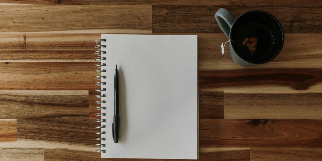 a notepad, pen, and cup of coffee on a wooden table