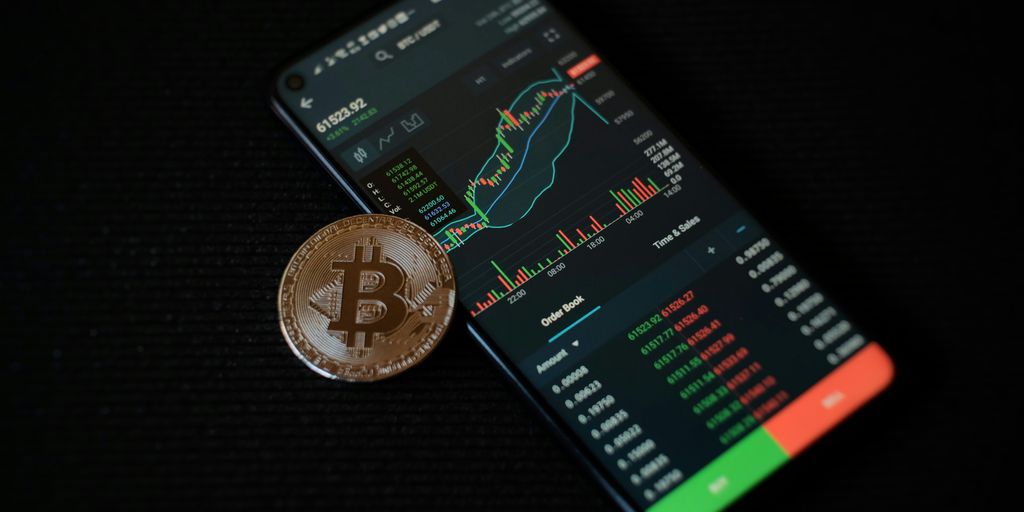A smartphone displaying cryptocurrency data next to a Bitcoin.