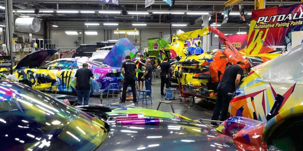 Workers painting cars in a bright automotive workshop.