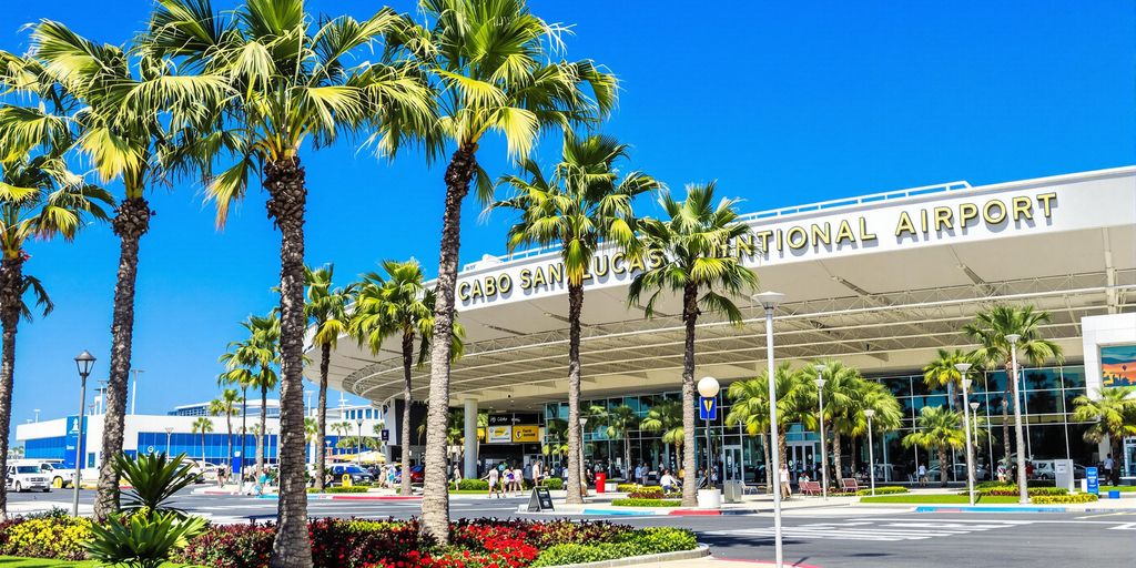 Cabo San Lucas International Airport with palm trees and travelers.