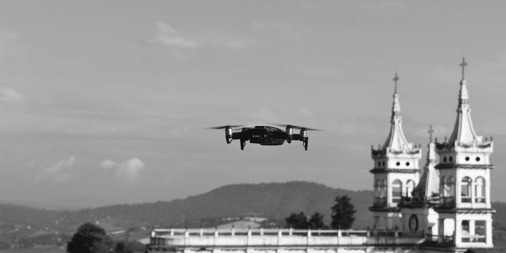 grayscale photo of black plane flying over white building