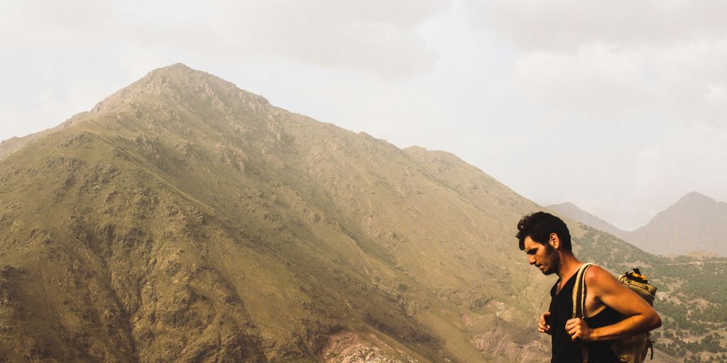 man carrying backpack standing near mountain