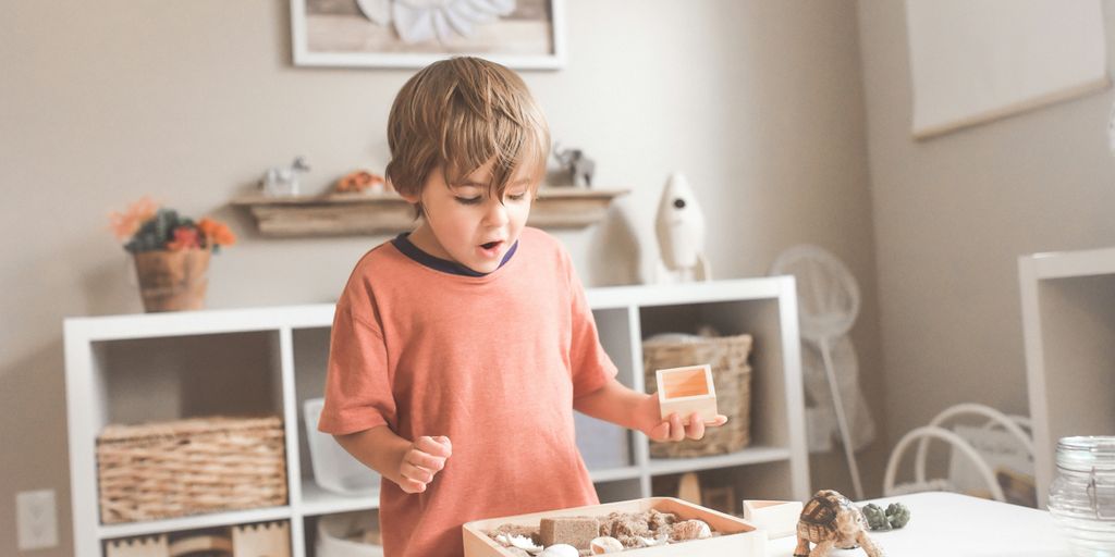 boy in orange crew neck t-shirt standing in front of white wooden table with cupcakes