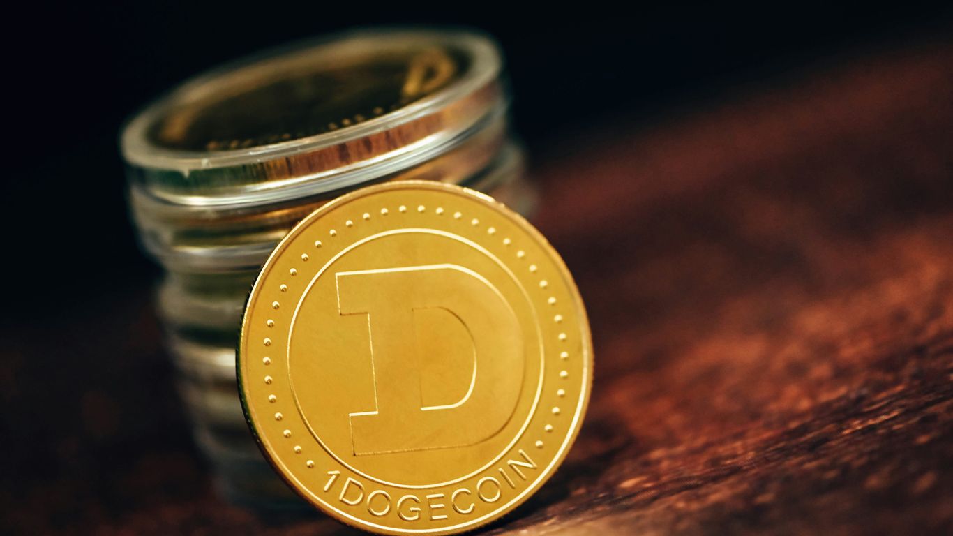 Dogecoin coin in front of stacked coins on wooden surface.