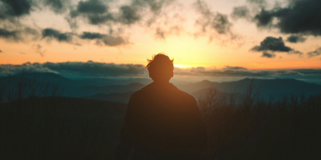 silhouette of man standing on mountain during sunset