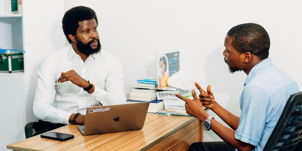 Two men sitting at a desk talking to each other