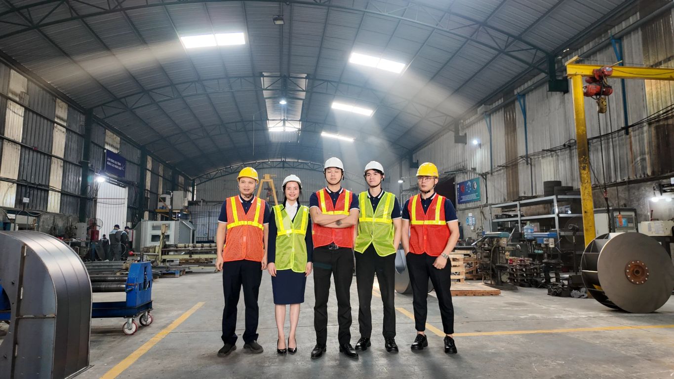 Five individuals in safety gear standing inside an industrial workspace.