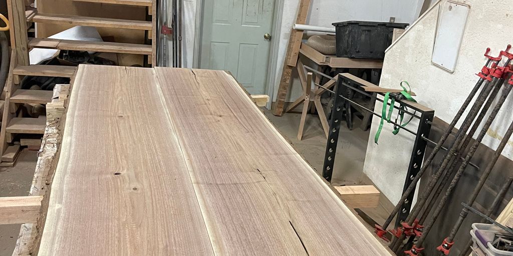 Wooden table in a workshop with stairs and tools nearby.