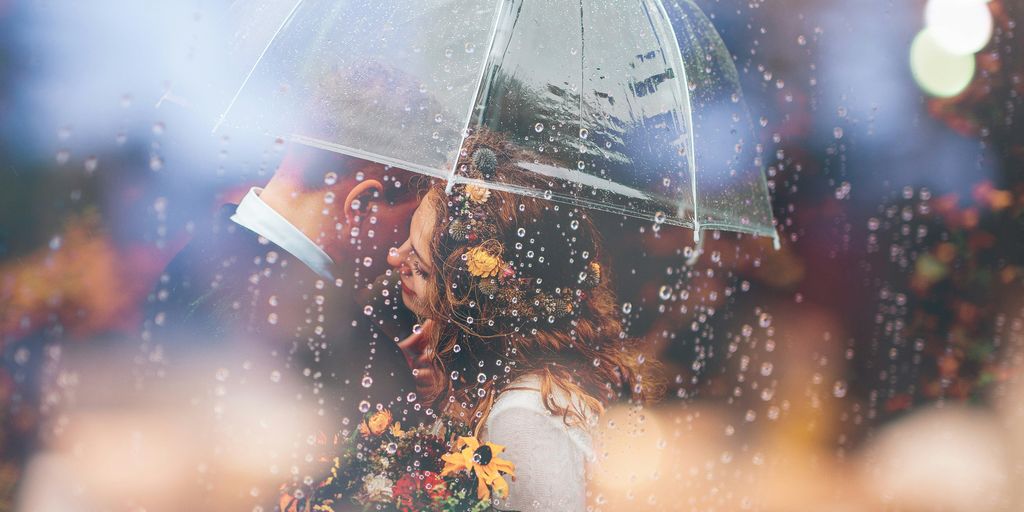 a bride and groom kiss in the rain under an umbrella
