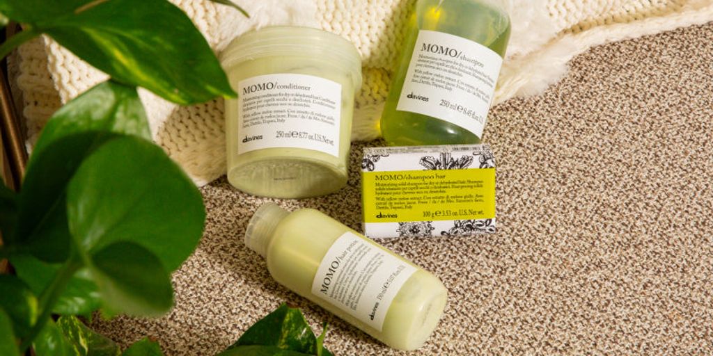 Haircare products displayed with plant and knitted fabric background.