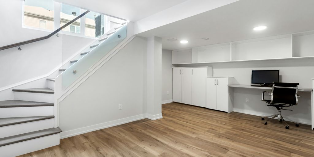 an empty room with a desk, computer, and stairs