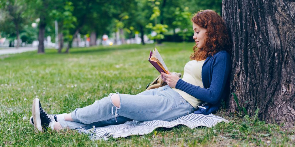 a woman sitting under a tree reading a book