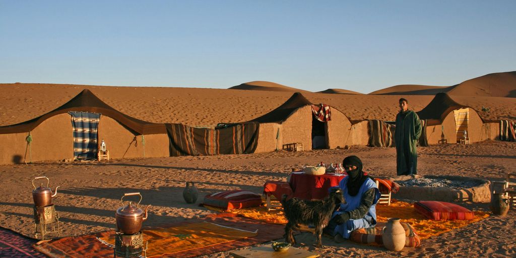 man sitting on carpet in desert floor near tents