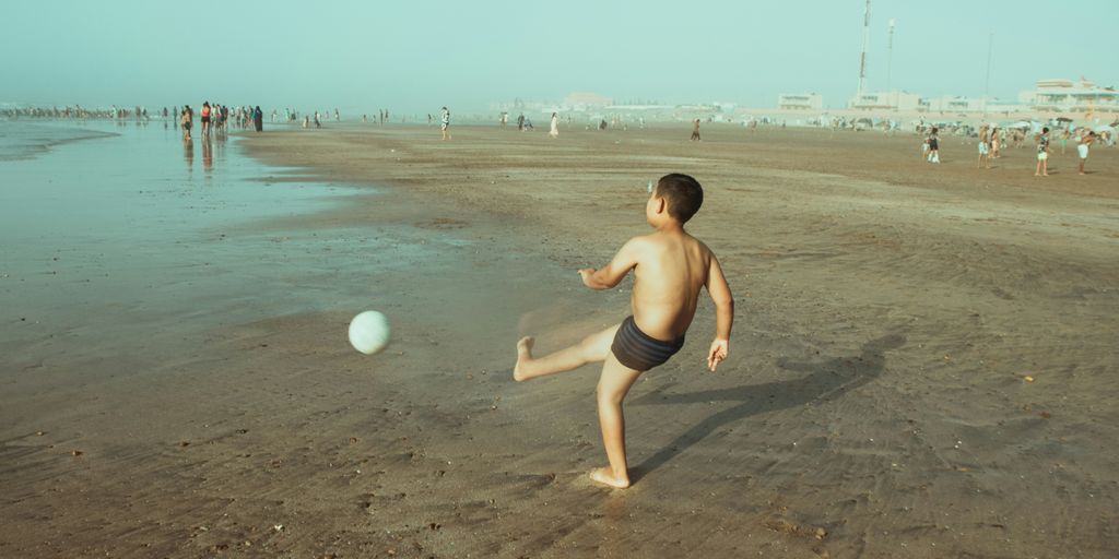 A young boy playing with a ball on the beach