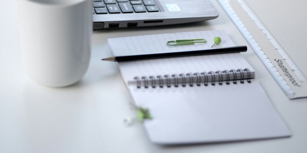 black pencil on ruled notepad beside white ceramic mug and gray laptop computer