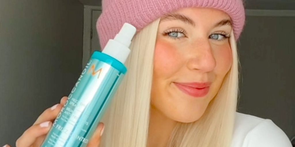 Woman holding a skincare product, wearing a pink beanie.