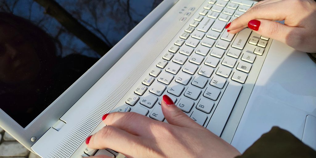 a woman is typing on a laptop outside