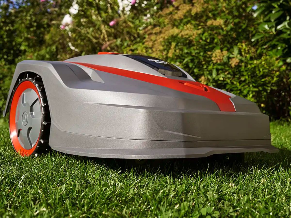 Robot lawn mower on green grass in a garden setting.