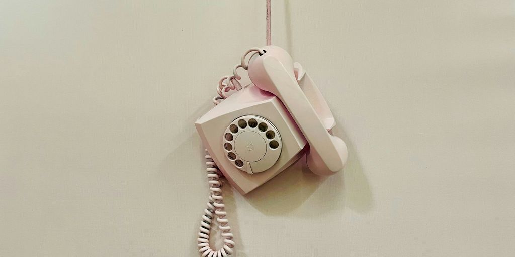 a pink phone hanging from a cord on a wall