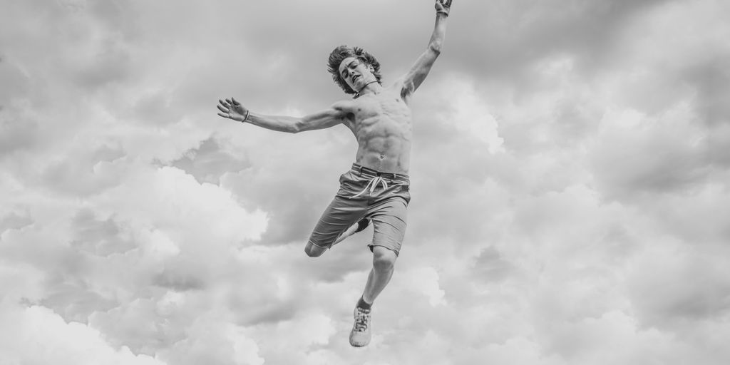 grayscale photo of person jumping overlooking clouds