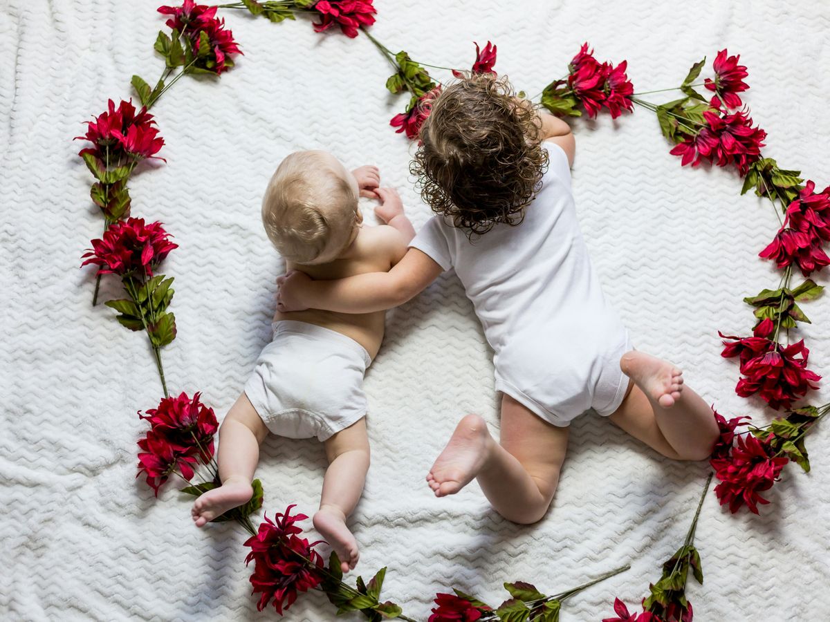 two baby's lying surrounded by red petaled flowers