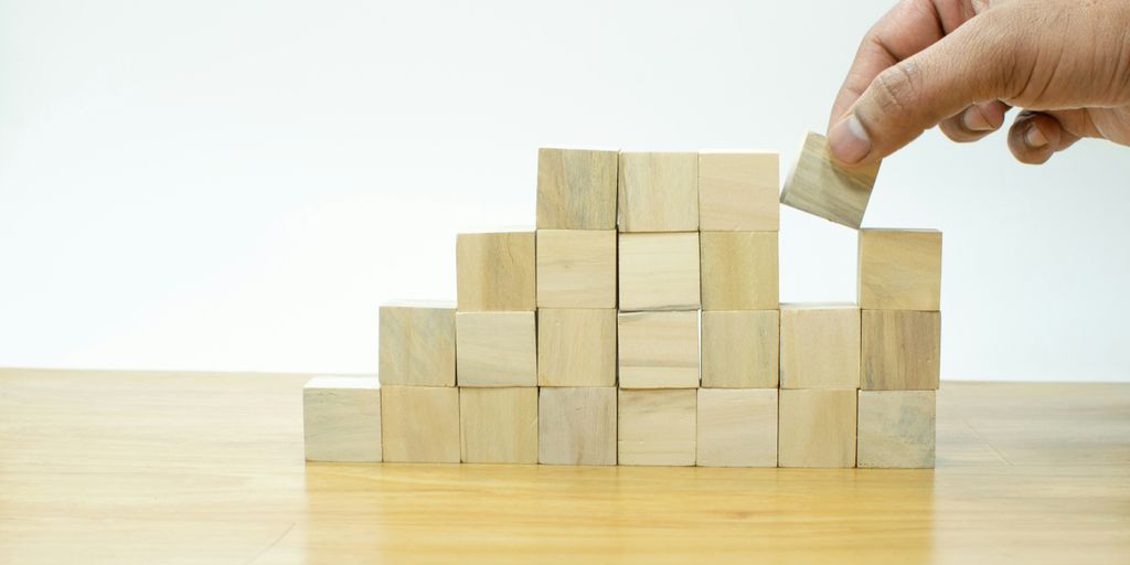 A person placing a block into a pile of wooden blocks