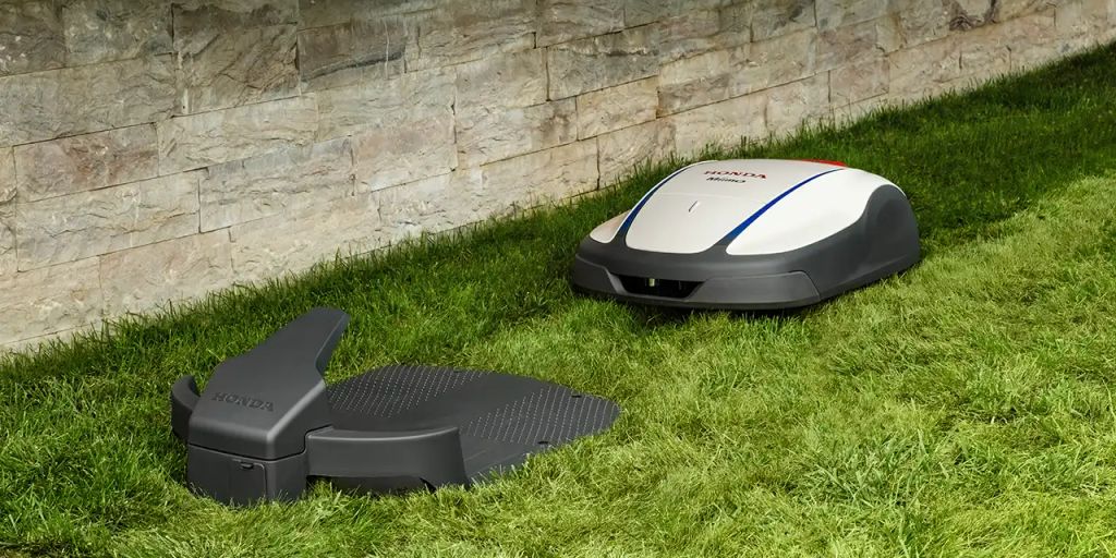 A robotic mower on grass next to its charging station.